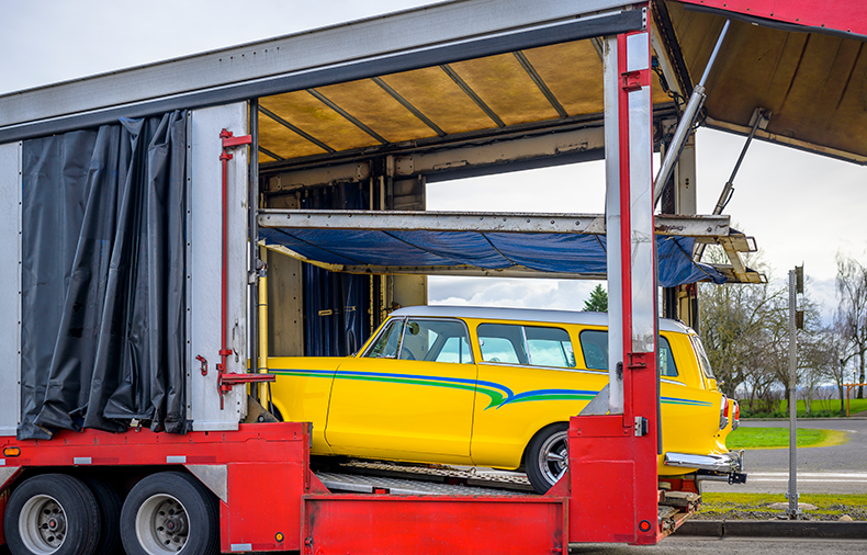 vintage yellow vehicle loading onto enclosed trailer - cost to ship a car cross-country
