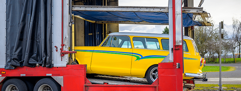 A yellow vintage vehicle being loaded for enclosed transport