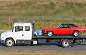 a red vintage car that was purchased through eBay motors being transported on a white truck driving on the highway